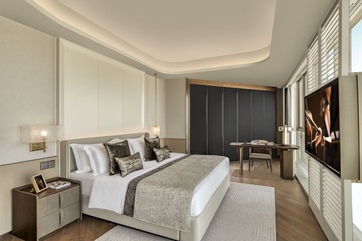 A modern bedroom with a large bed, bedside tables, a desk, and a TV.
