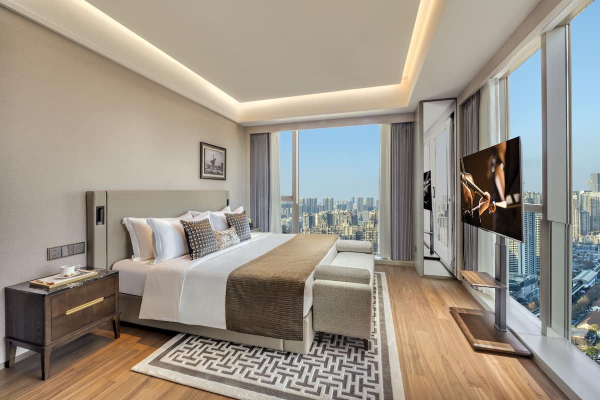 A modern hotel room with a large bed, a TV, and a city view.