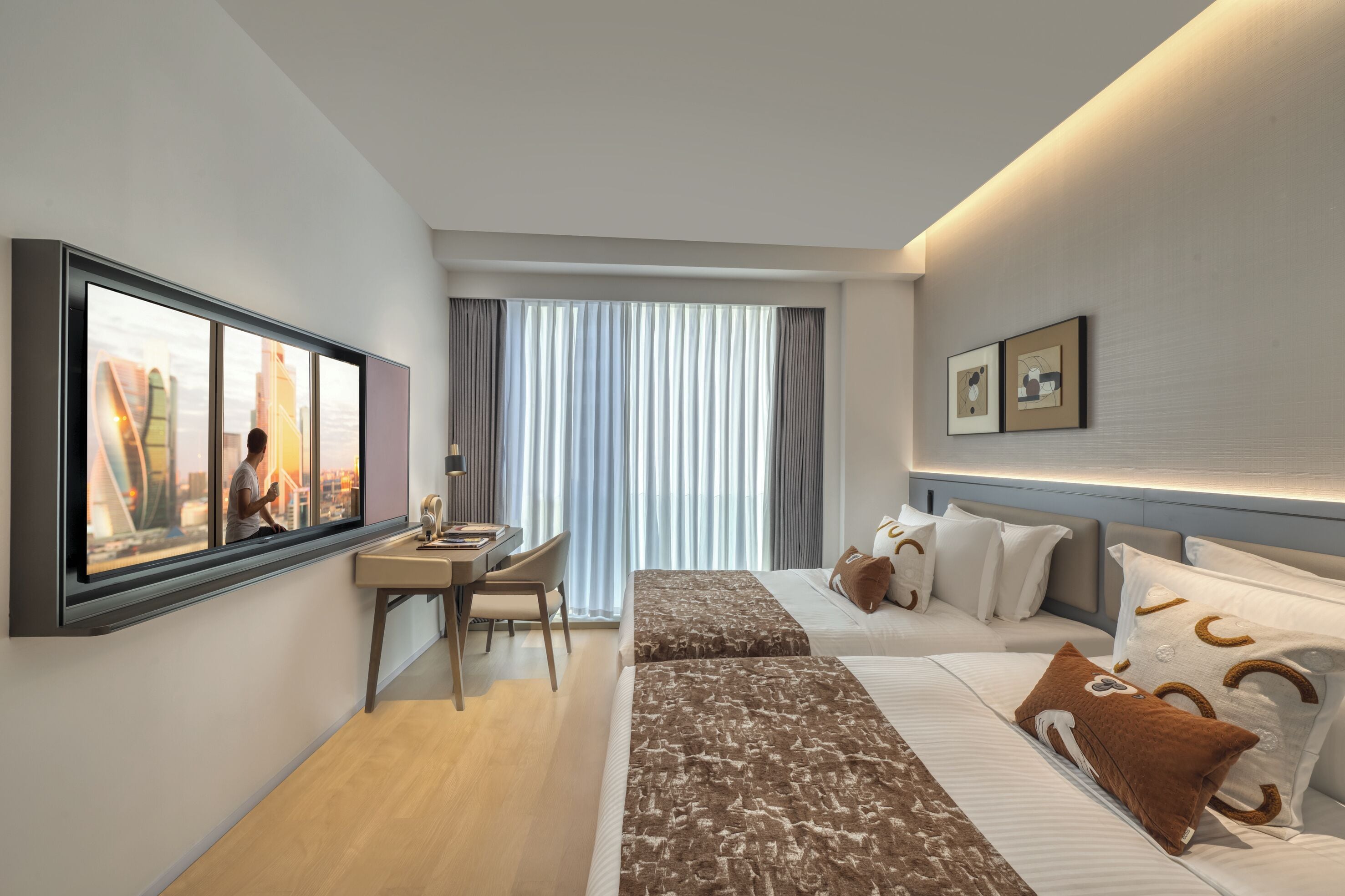 Una habitación de hotel moderna con escritorio, dos camas, un ventanal con cortinas y obras de arte en las paredes.