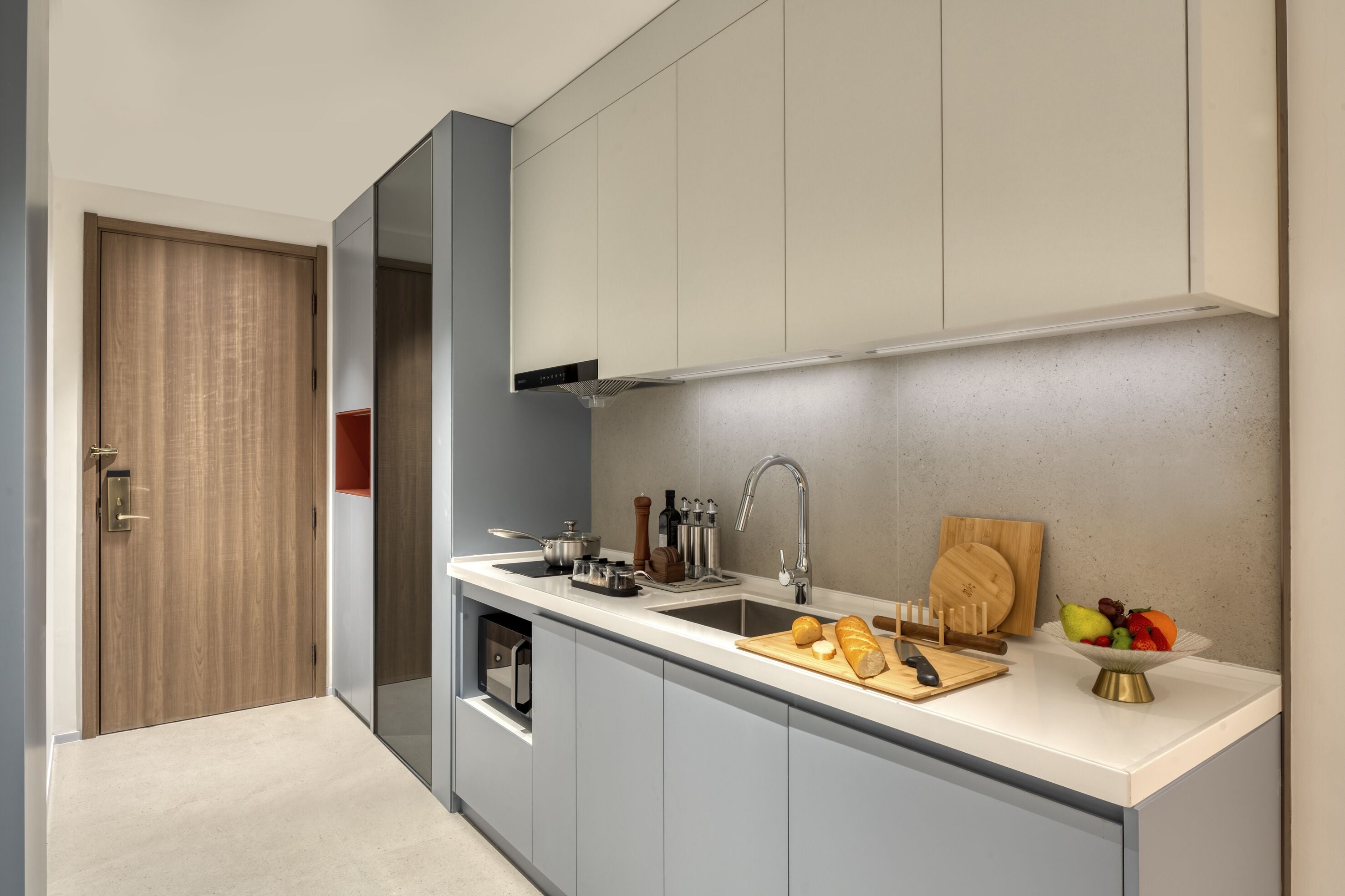 A modern kitchen with a built-in oven, a sink, and a cutting board with bread and fruit.