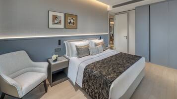 A modern hotel room with a large bed, a nightstand, a chair, and a wardrobe.