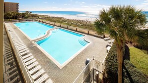 Une piscine avec vue sur la plage, un palmier et un bâtiment en arrière-plan.
