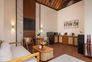 A modern interior with a sofa, wooden furniture, a dining table, a kitchen area, and a wall-mounted artwork. - The Prime Seminyak (Kerobokan)