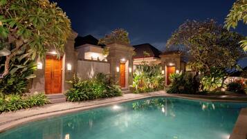 A pool area with a clear pool, surrounded by lush greenery and a building with multiple doors.