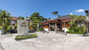 L’entrée d’un hôtel, avec une enseigne, un chemin pavé et de la verdure environnante.