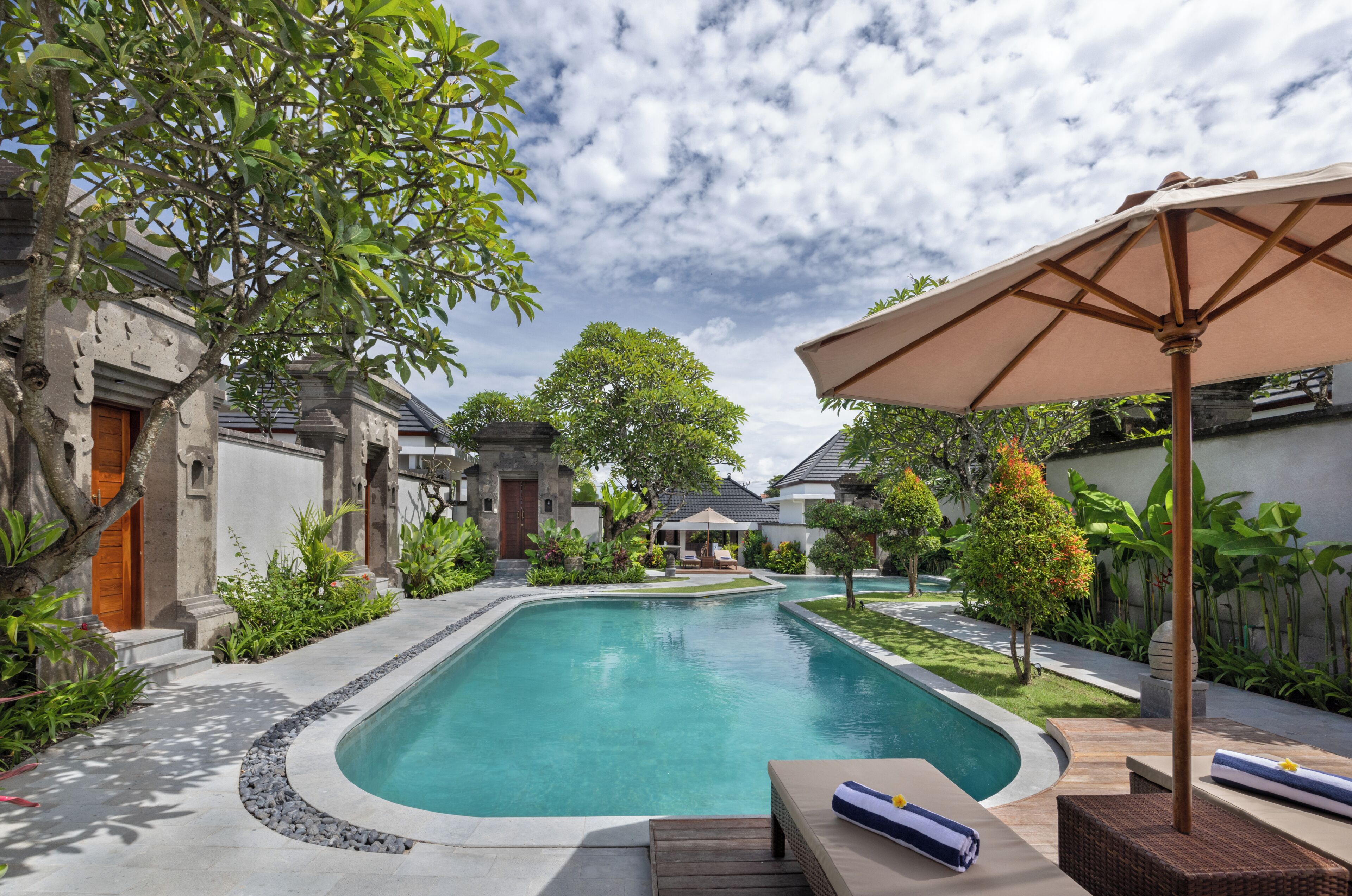 A swimming pool with a wooden deck, lounge chairs, and a pergola with an umbrella.