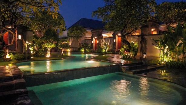 Un espace piscine nocturne comprenant plusieurs bassins, entouré d’arbres et éclairé par un système d’éclairage d’ambiance.