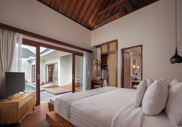 A bedroom with a bed, a TV, a wooden dresser, and a view of a pool. - The Prime Seminyak (Kerobokan)