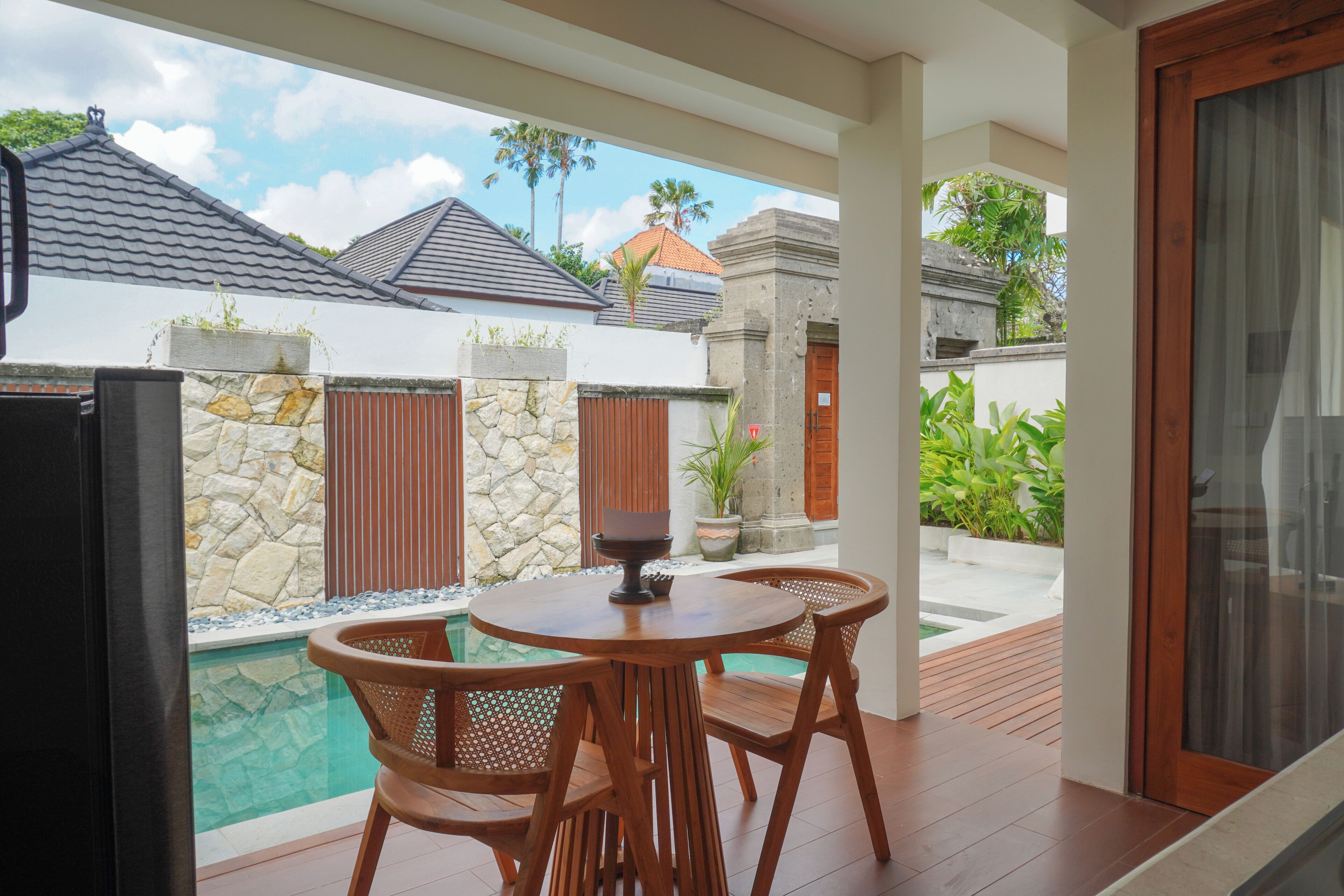 A covered outdoor area with a pool, wooden furniture, and stone walls.
