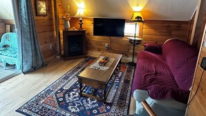 A cozy cabin interior with a wooden floor, a sofa, a coffee table, a TV, and two lamps.