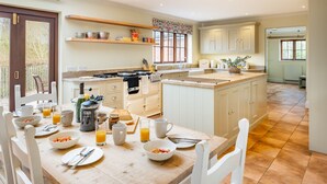 A spacious kitchen with white cabinetry, a dining table set for breakfast, and a large island with a sink. - Tuffon Hall Farmhouse, Sible Hedingham, Suffolk (Sible Hedingham)