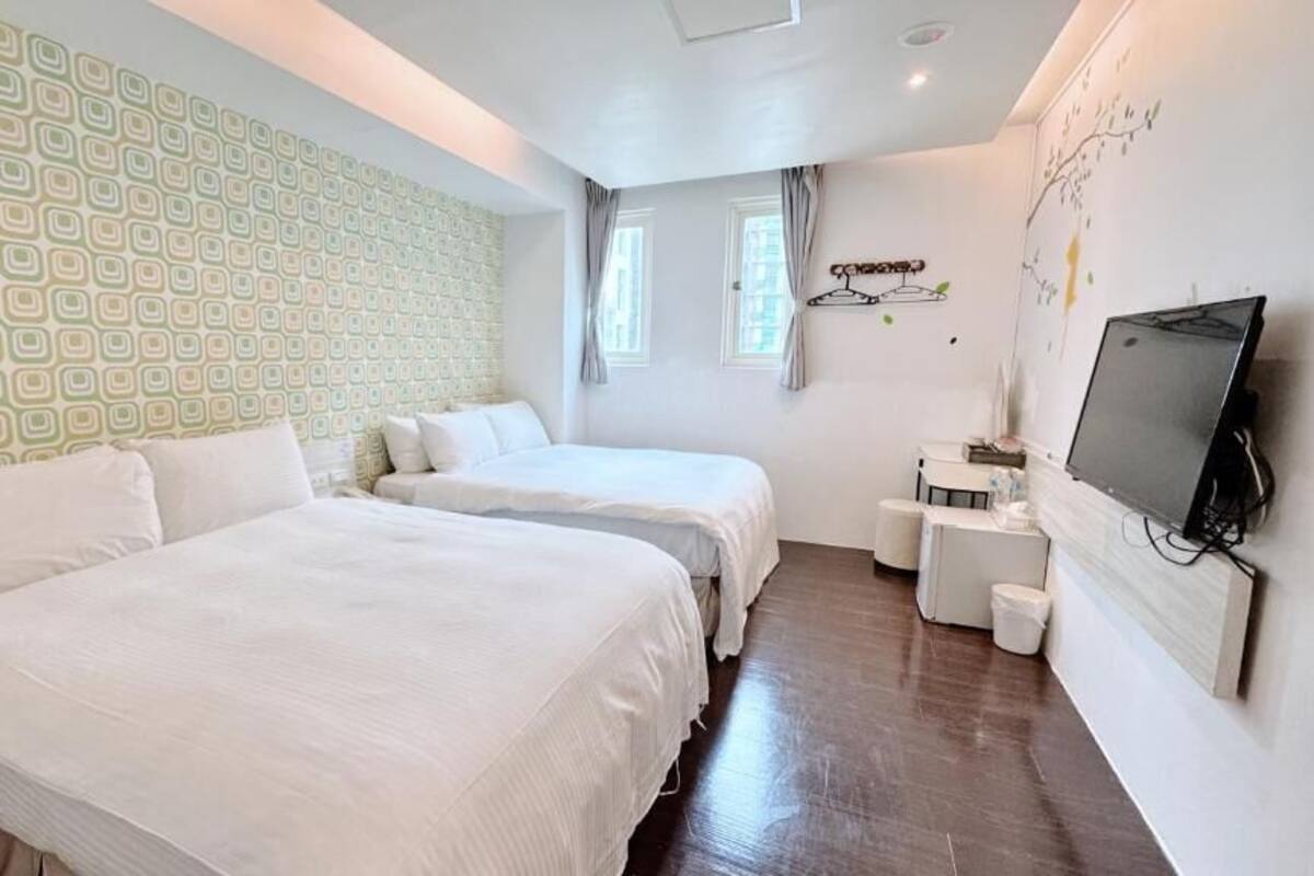 Ein Hotelzimmer mit zwei Betten, einem Fernseher, einem kleinen Schreibtisch und einem Fenster mit Vorhängen.