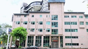 A multi-story building with a prominent sign at the top, large windows, and a visible entrance with a sign. - Yoai Jiaoxi Spring Hotel (Jiaoxi)
