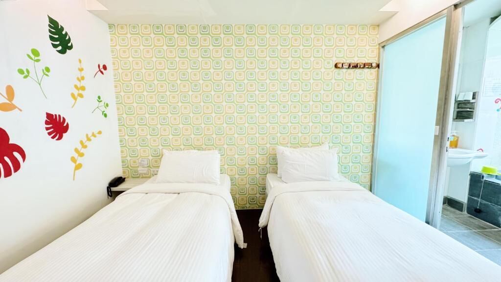 Una habitación con dos camas individuales, un papel tapiz decorado y un baño visible a través de una puerta corredera.