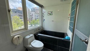 A bathroom with a toilet, a bathtub, a window, and a view of buildings outside. - Yoai Jiaoxi Spring Hotel (Jiaoxi)