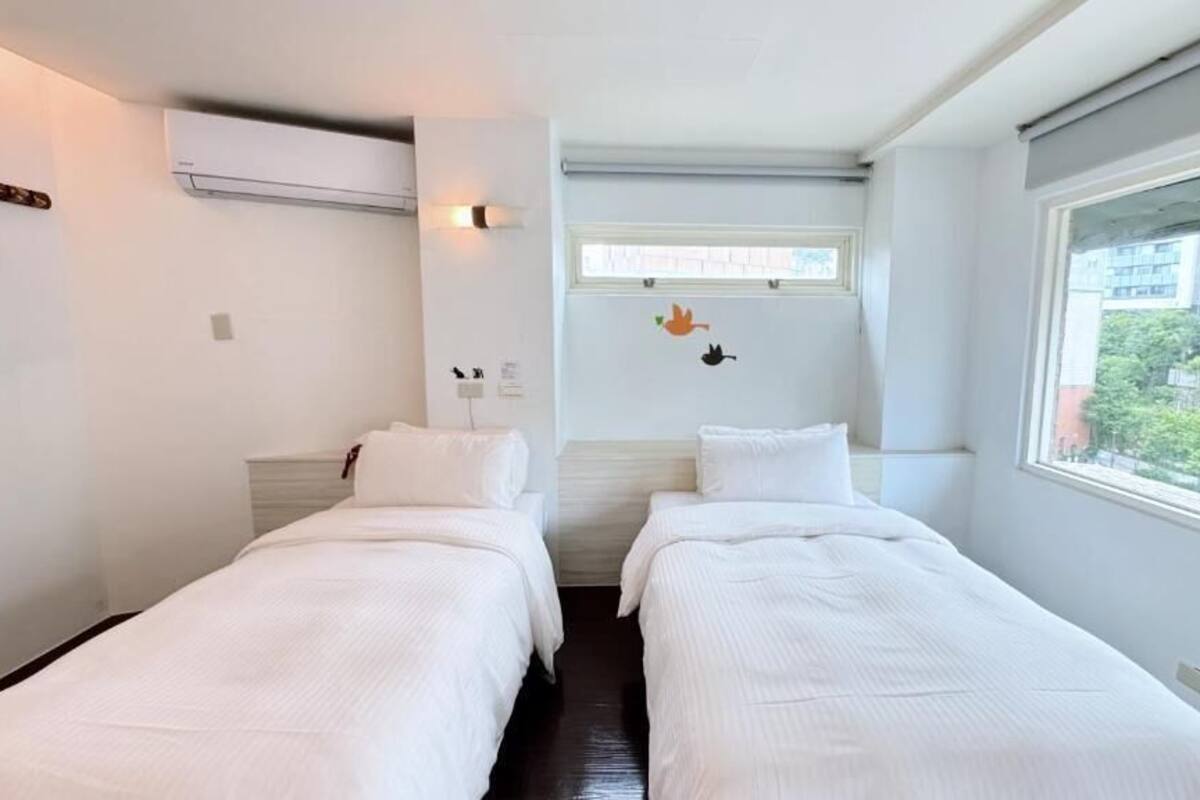 Ein Doppelzimmer mit zwei Betten, einem Fenster und einer Wand-Klimaanlage.