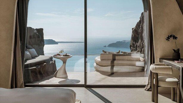 A modern room with a large sliding glass door leading to a balcony with a view of the sea and cliffs. - One of One - Adults Only (Santorini)