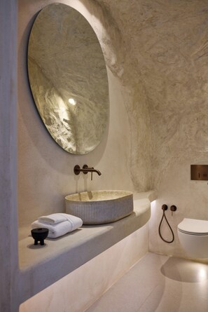 A bathroom with a marble sink, a large mirror, a toilet, and a towel on the counter. - One of One - Adults Only (Santorini)