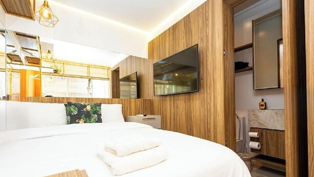 Ett modernt hotellrum med en stor säng, träpanel på väggarna, en platt-TV och ett badrum med en bänkskiva i marmor.