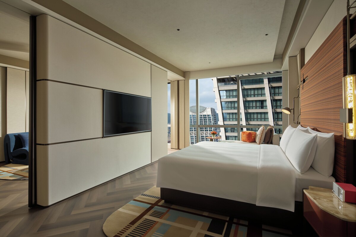 Camera d'albergo moderna con un letto grande, una TV a schermo piatto, vista sulla città e un balcone con panorama urbano.