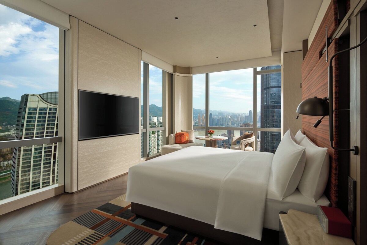Una moderna camera d'hotel con un letto grande, una TV a schermo piatto, vista sulla città e un balcone.