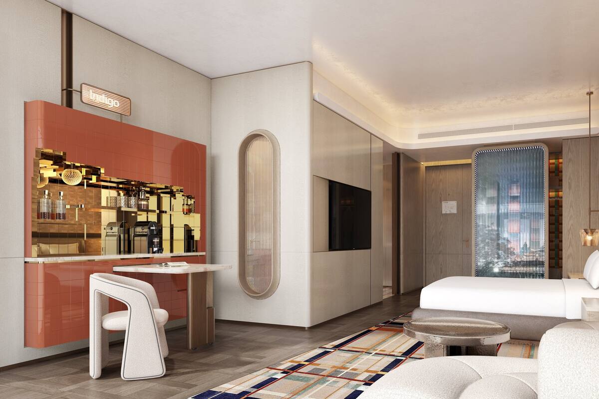 A modern hotel room with a bed, seating area, a minibar, and a large mirror.