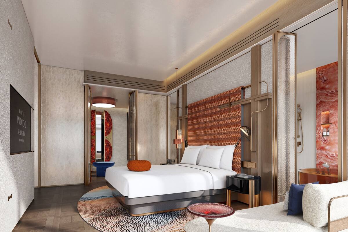 A modern hotel room with a large bed, a round coffee table, and a view of the city.