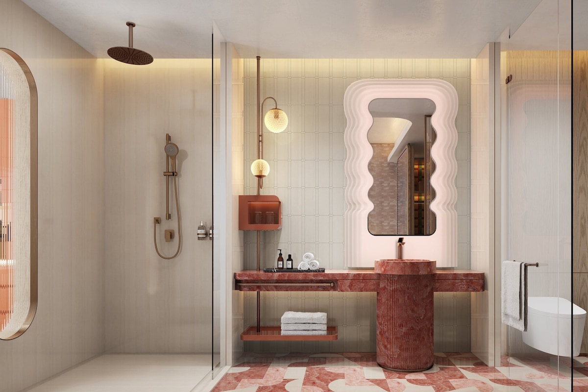 A modern bathroom with a glass shower enclosure, a marble vanity, and a large mirror with a unique wavy frame.