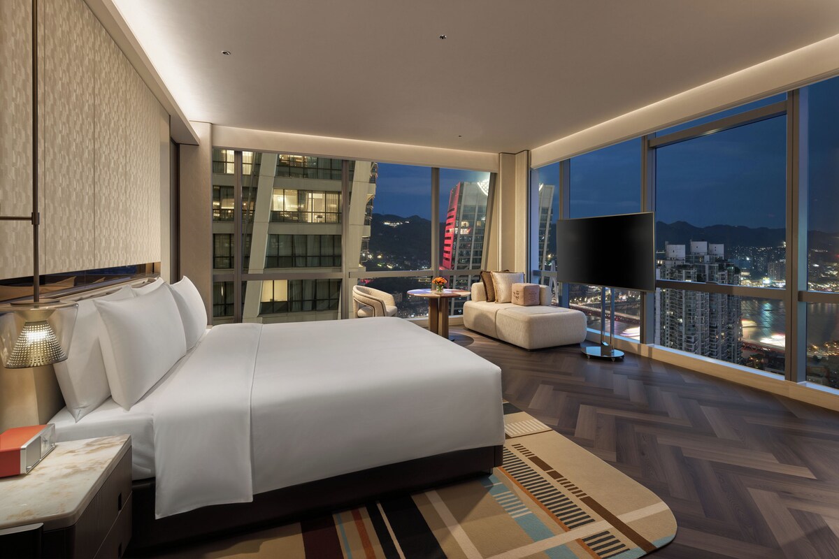Camera d'albergo moderna con un letto grande, un angolo salotto e vista sulla città.