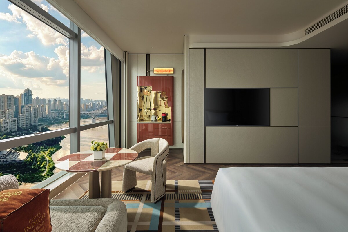 Una moderna camera d'hotel con una grande finestra, una TV a schermo piatto, un divano, un tavolo da pranzo e vista sulla città.