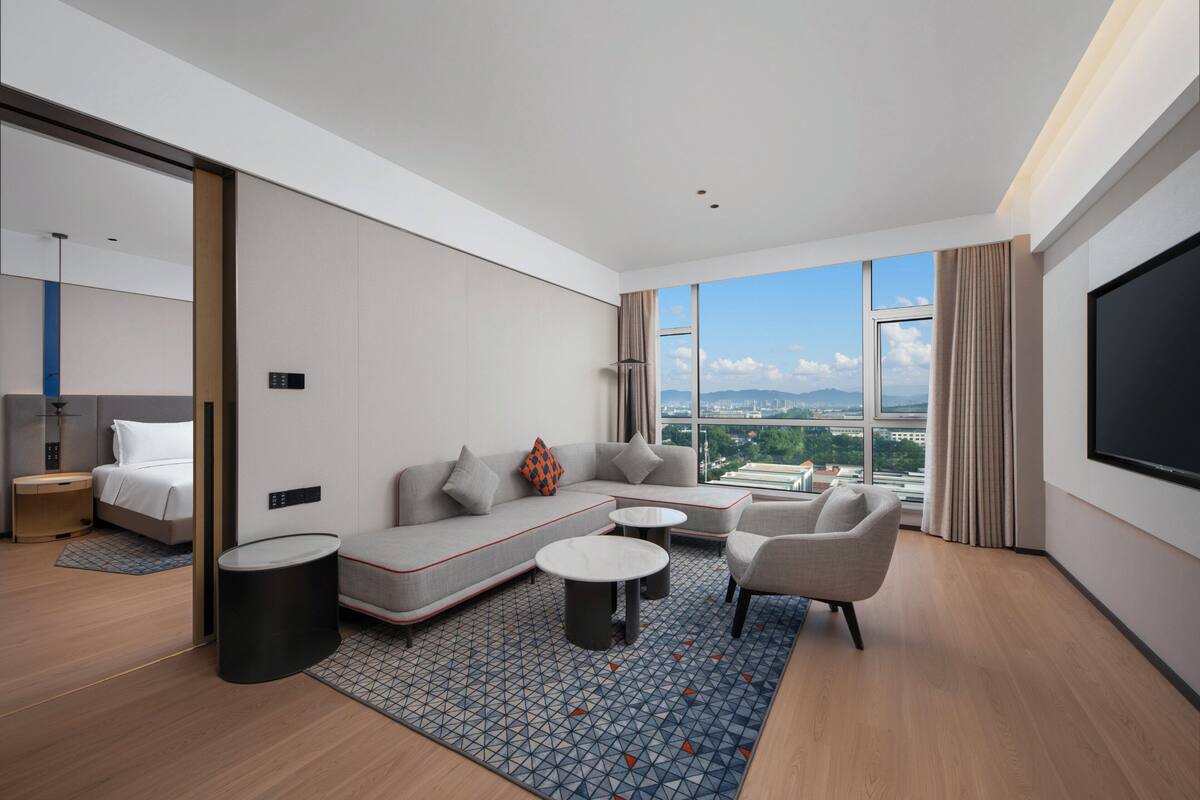 Ett modernt hotellrum med en säng, soffa, fåtölj, soffbord och en stor TV-skärm.