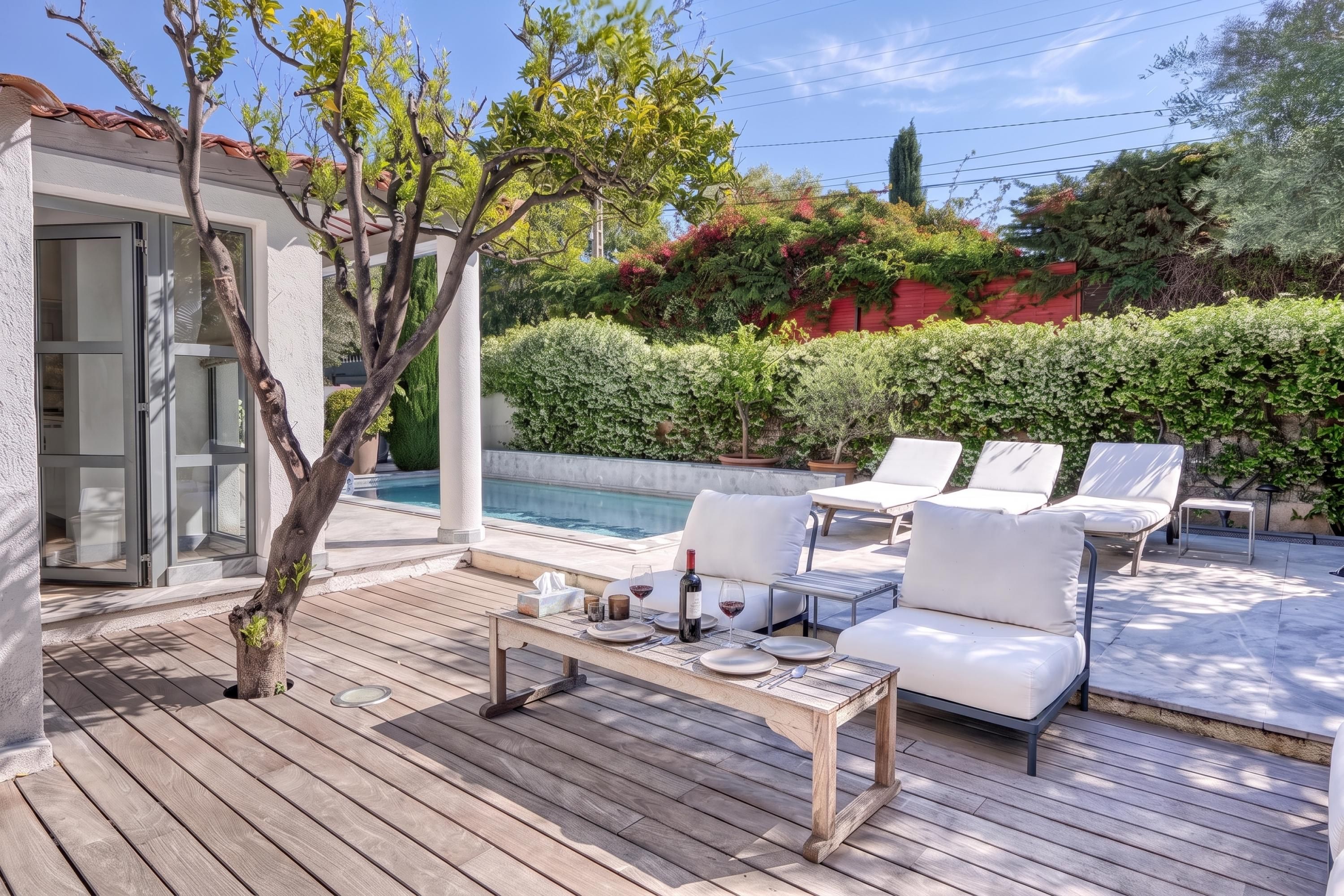 An outdoor deck with a pool, lounge chairs, and a dining table set for two.