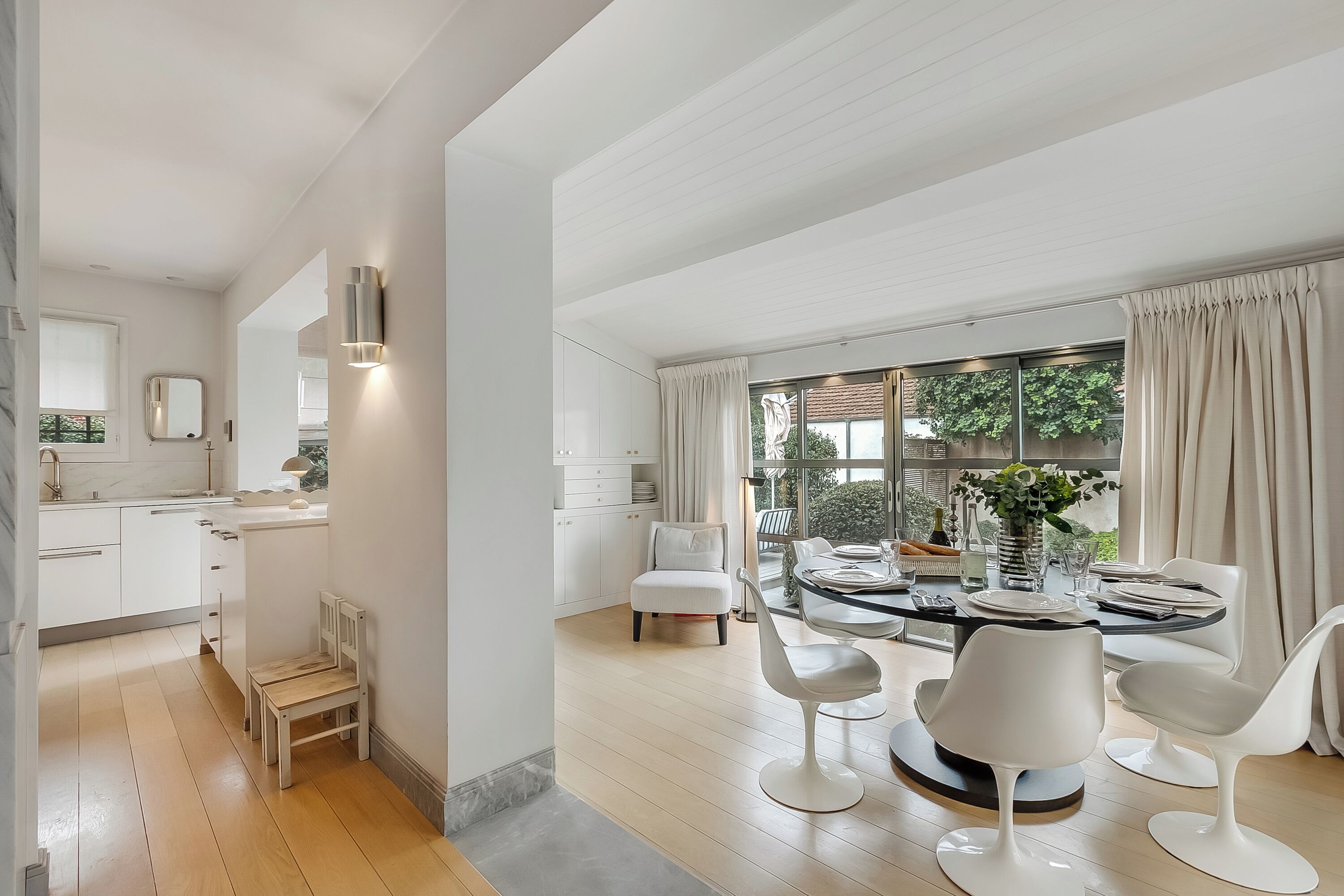 A modern kitchen with white cabinets, a wooden chair, and a dining area with a round table and white chairs.