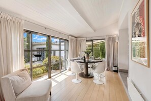 A modern dining area with a round table, white chairs, and a view of the outdoors through large windows. - Cap d'Antibes Villa - Close To The Beach, Antibes, France (Antibes)