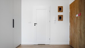 Ein Zimmer mit einer weißen Tür, einem Holzschrank, einer Bank und zwei gerahmten Bildern an der Wand.