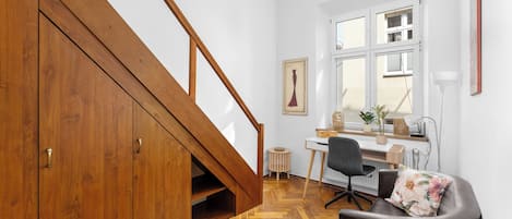 Una habitación con una escalera de madera, un escritorio con computadora, una silla y una ventana con persianas.