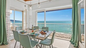 A dining area with a view of the sea, a table set with plates, glasses, and cutlery, and green chairs. - Holiday On The Sea - Seafront Apt, Menton, France (Menton)