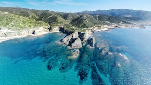 Vista aérea de un paisaje costero con aguas azules cristalinas, formaciones rocosas y colinas verdes.