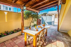 A covered patio with a wooden table and chairs, a tiled floor, and a wall with a window and plants. - Favoloso Salento - Apartment with Balcony 50m to Beach, Maruggio, Italy (Maruggio)