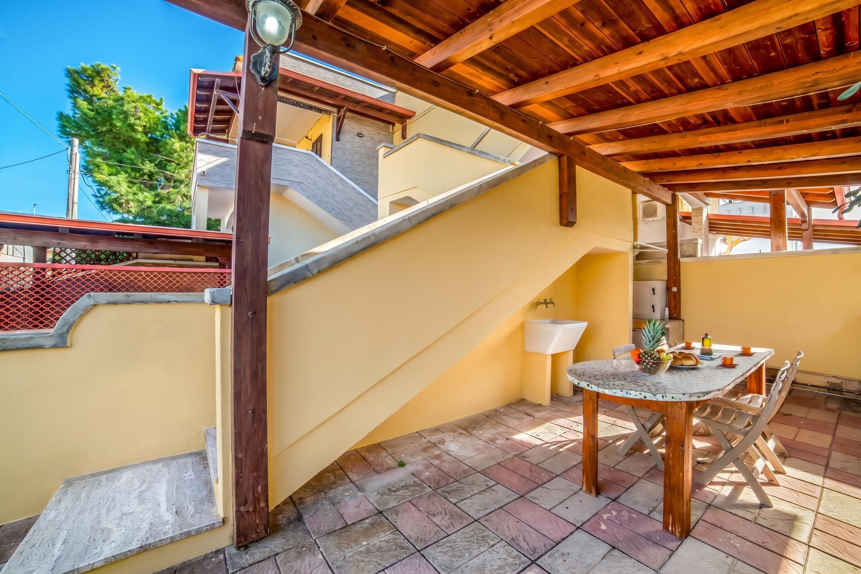 Un espacio al aire libre techado con una mesa y sillas, una escalera y vista a un edificio al fondo.