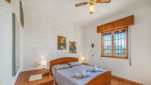 Une chambre à coucher avec un lit en bois, deux tables de chevet, un ventilateur de plafond et une fenêtre avec des barreaux.