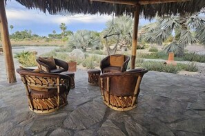 A covered outdoor seating area with wicker furniture and a view of a landscaped garden with palm trees. - Rancho La Trinidad, 8-acre ranch, walk to town. (Todos Santos)
