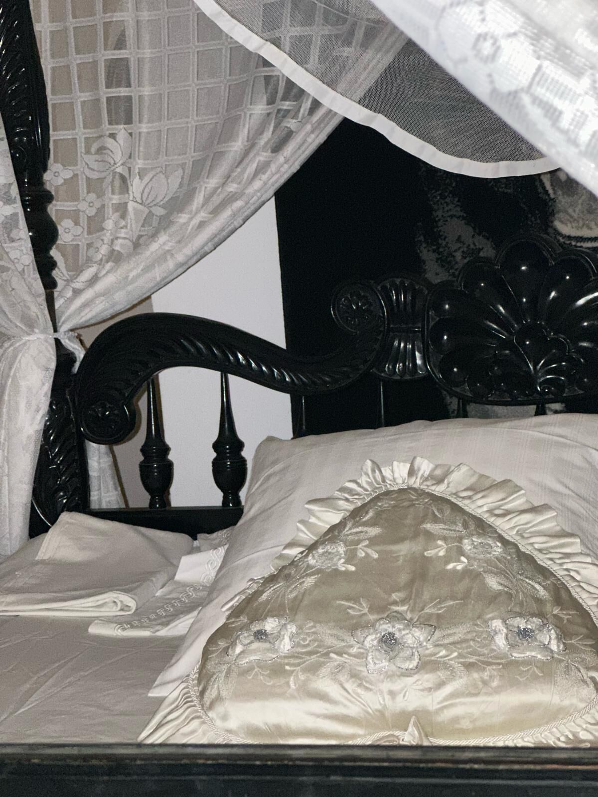 Ein Bett mit Baldachin, Kopfteil und einem Kissen mit Blumenstickerei.
