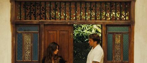 A couple holding hands at a doorway with intricate wooden designs and a tiled floor.