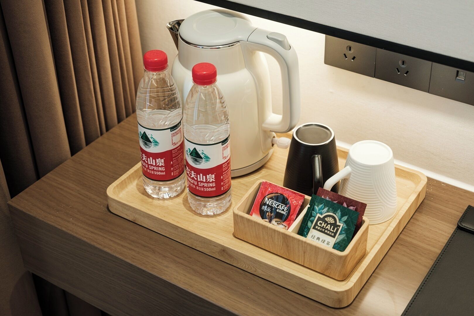 A wooden tray with two water bottles, a coffee pot, a mug, and a box of tea bags.