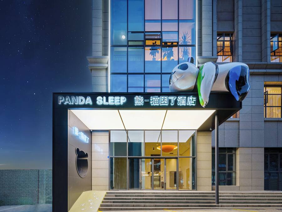 A hotel entrance with a sign reading 'Panda Sleep,' a bear logo, and a modern building facade.