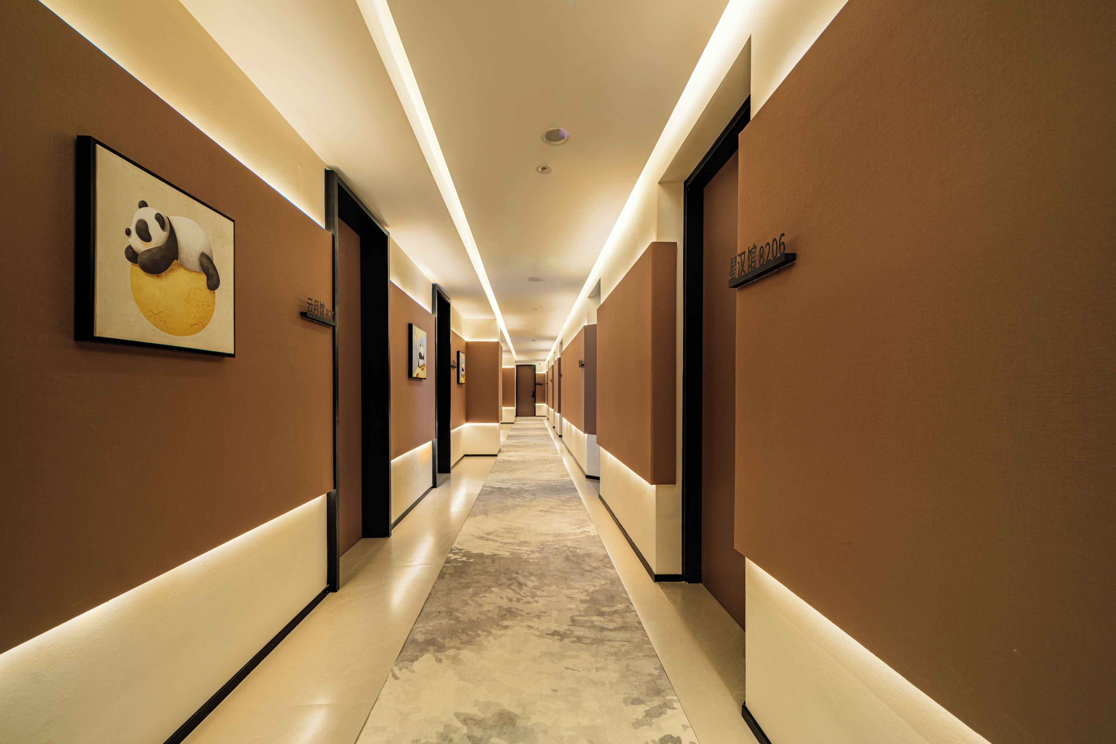 Un pasillo de hotel largo, con puertas a ambos lados y una obra de arte de panda en la pared izquierda.