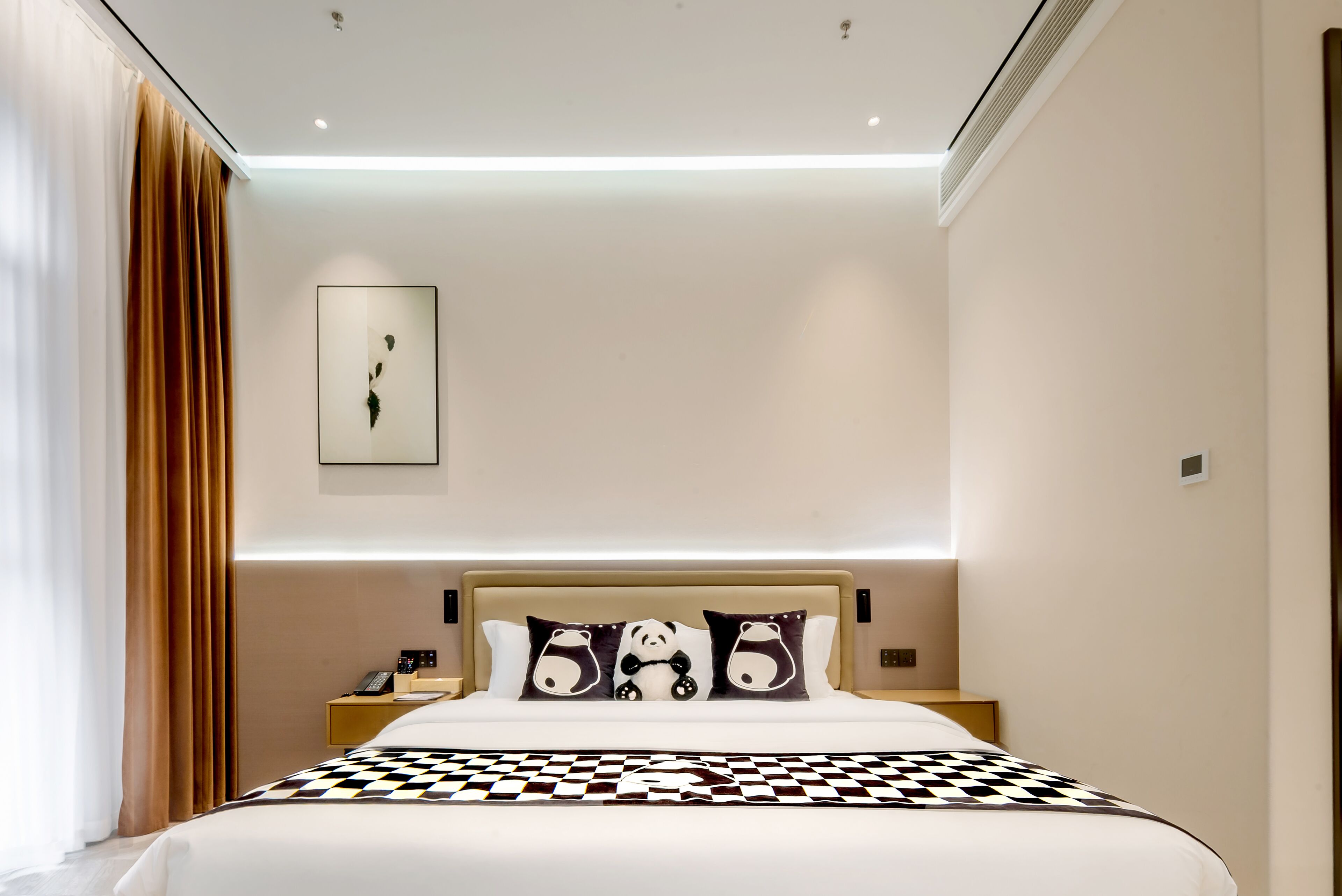 A modern hotel room with a large bed, a bedside table with a lamp, a wall-mounted artwork, and a window with curtains.