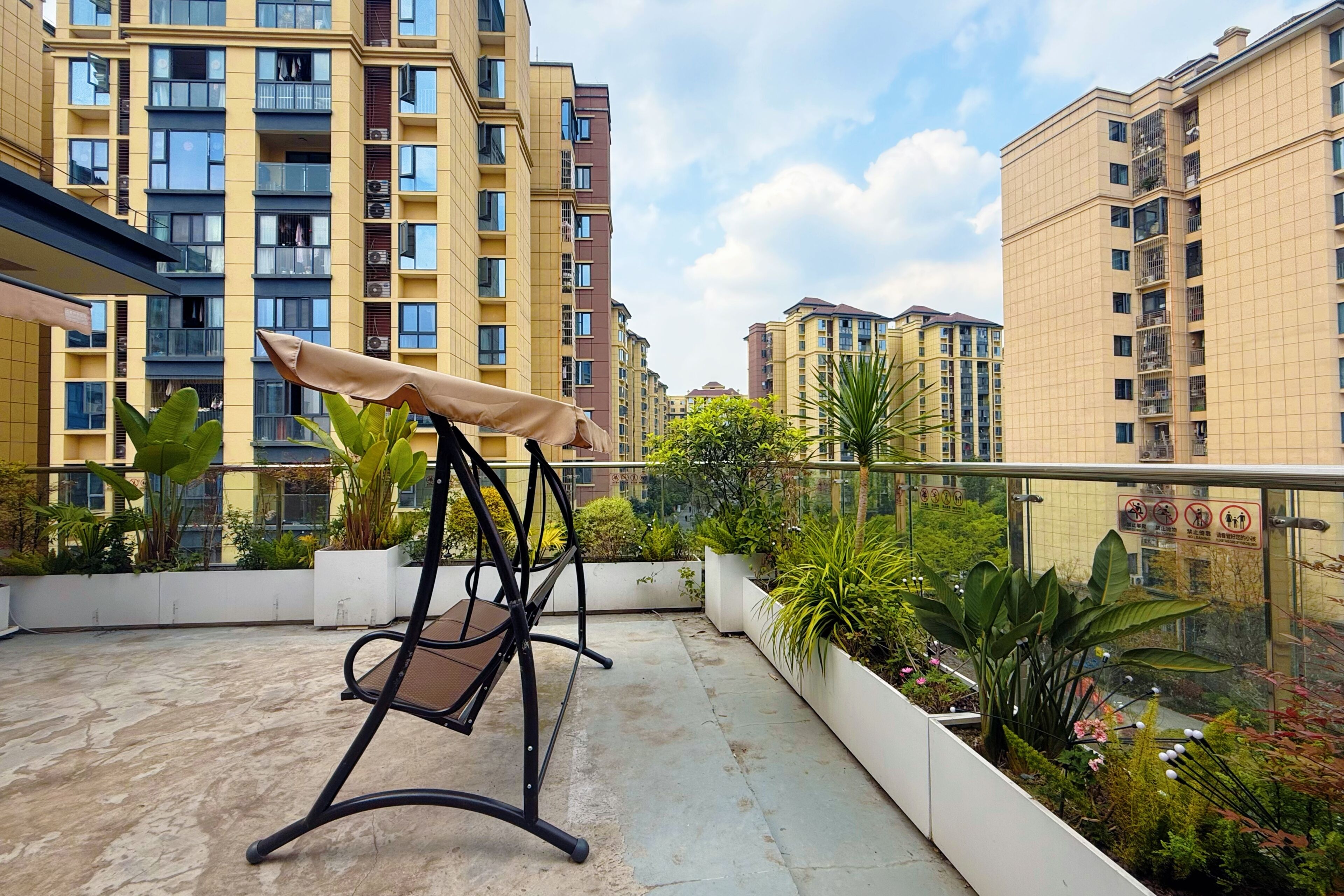 A balcony with a swing chair, potted plants, and a view of high-rise buildings.