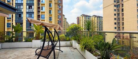 A balcony with a swing chair, potted plants, and a view of high-rise buildings.